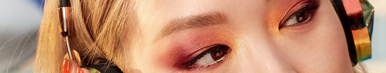 Ілюстративне зображення банера «Тіні для повік Maybelline New York» — фото крупним планом жінки-азійки з білявим волоссям у навушниках, нафарбованої яскравими тінями для повік